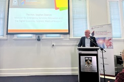 Minister Dawson presenting at the FHRI Fund Open Day. He stands behind a podium with a projector screen behind him to his right